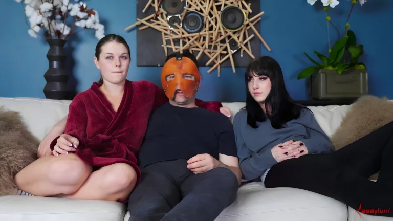 Two Beautiful Girls And A Masked Man Sit And Talk On The Couch 